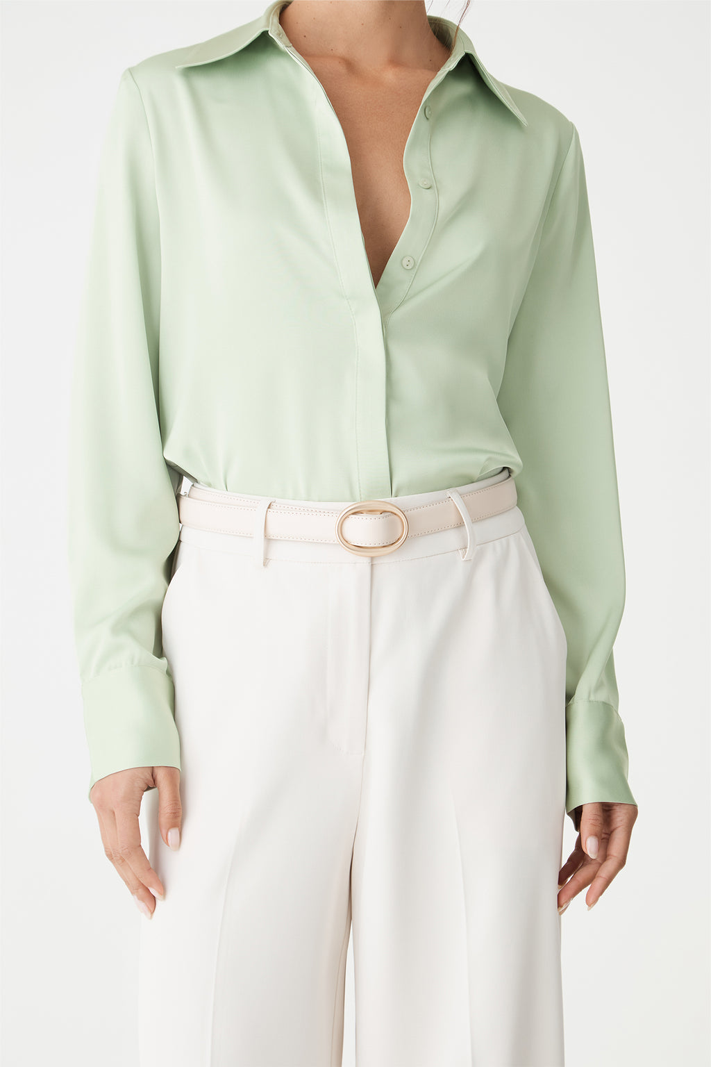 Detail of the mint satin shirt cuff and hem tucked into belted cream trousers
