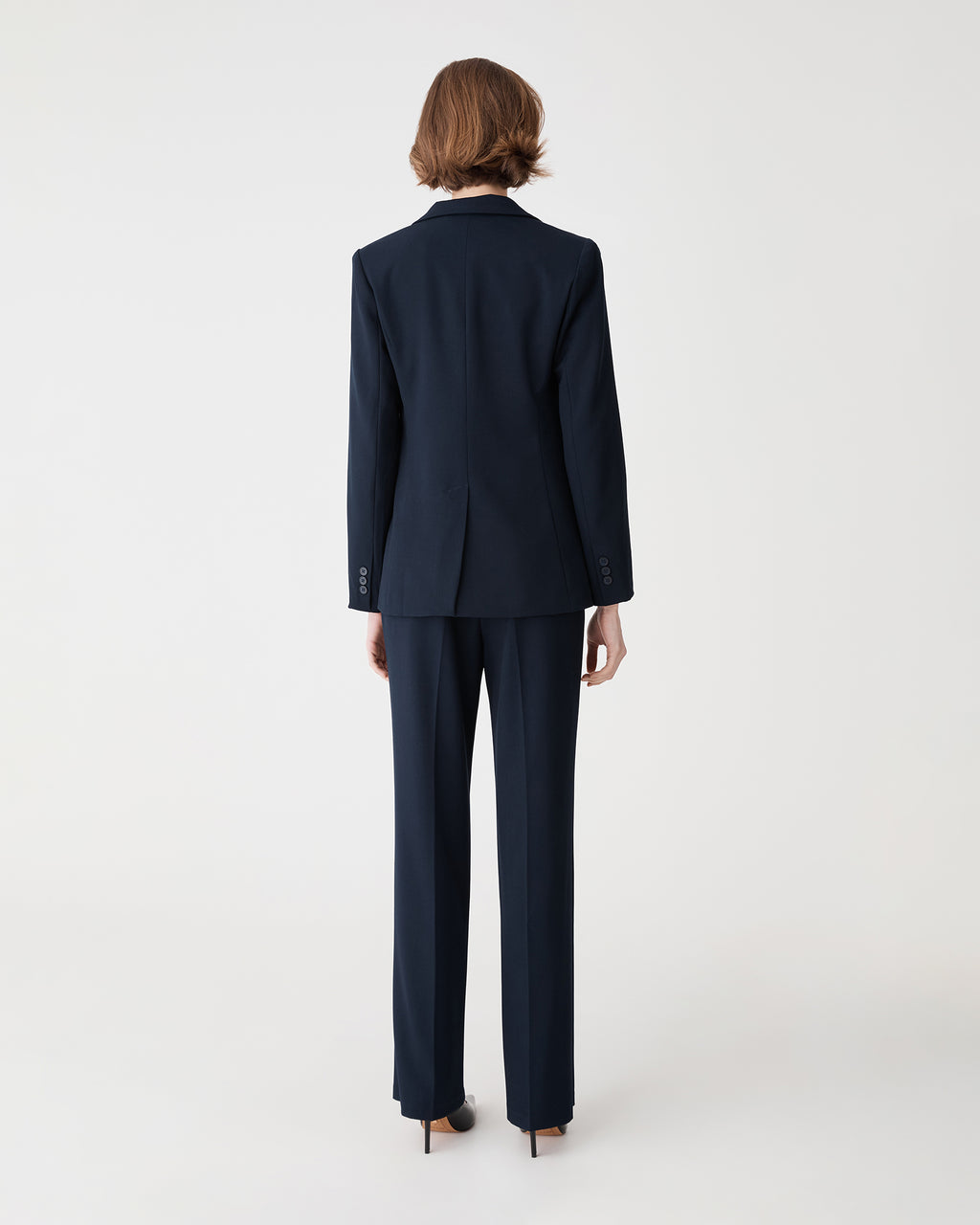 Back view of the navy blazer showing the back vent, worn with matching pants