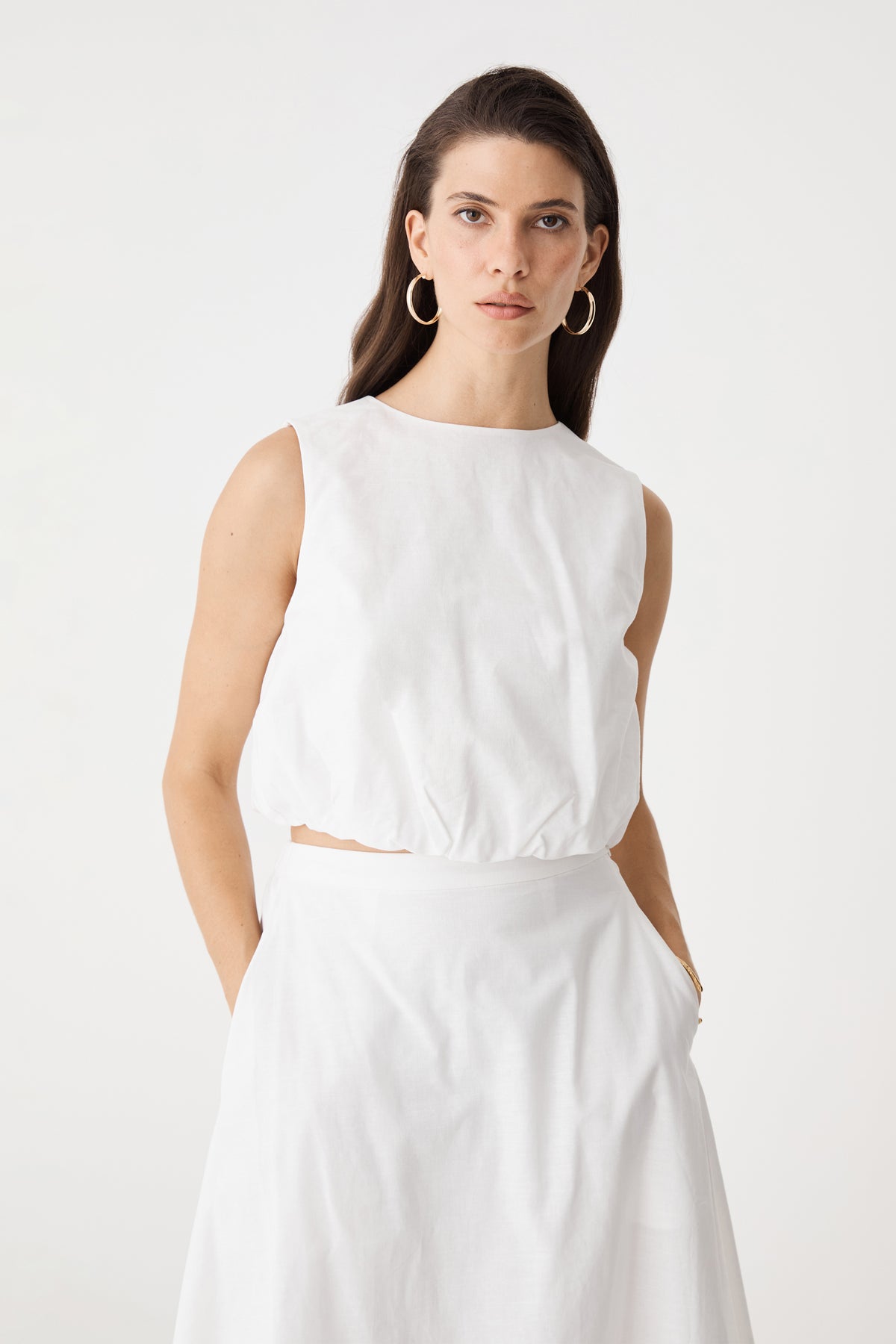 Close-up front view of the ivory sleeveless top with round neckline and cropped bubble hem