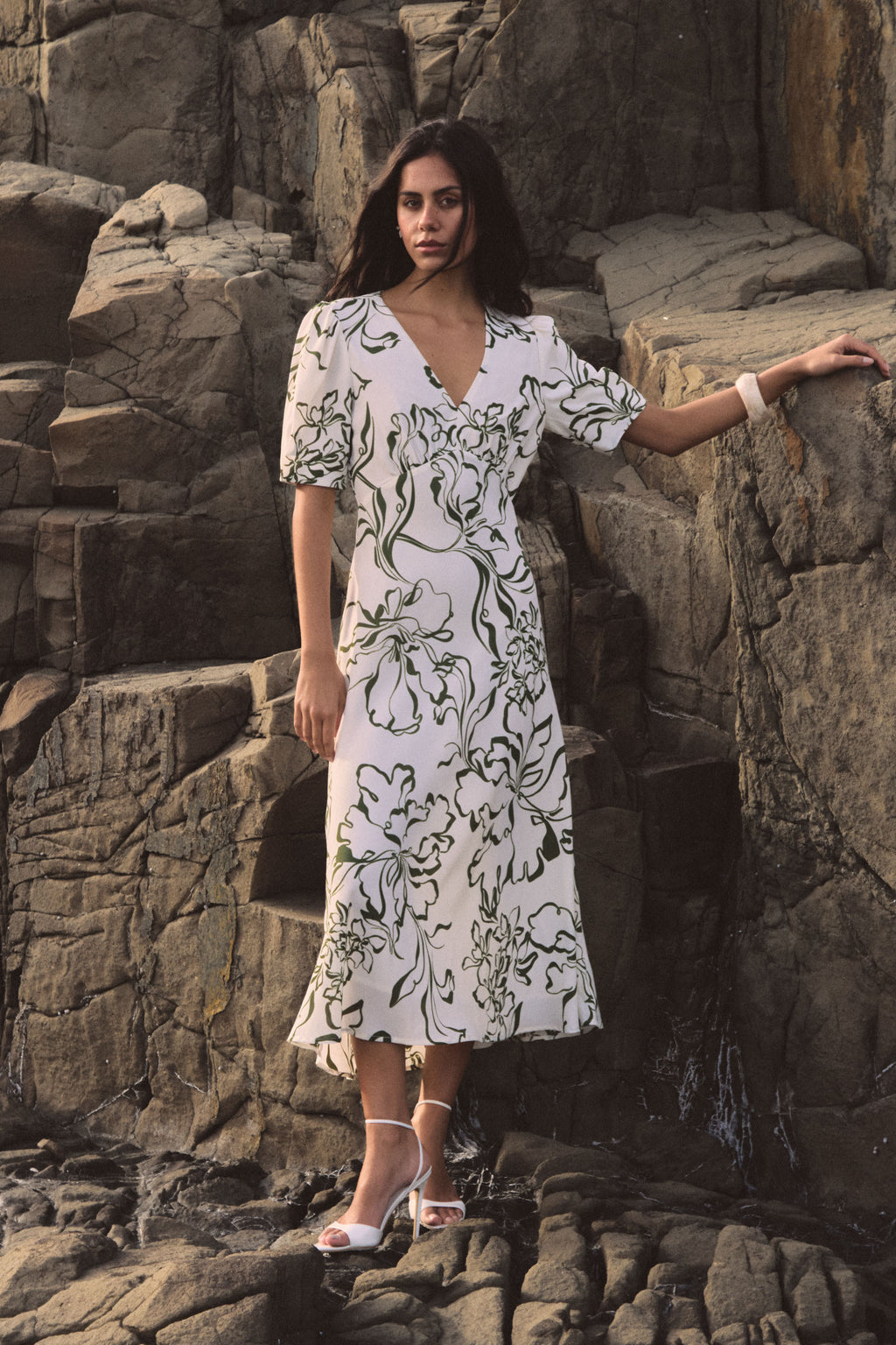 Natalie V-Neck Floral Dress in cream and olive floral print, worn standing on rocks