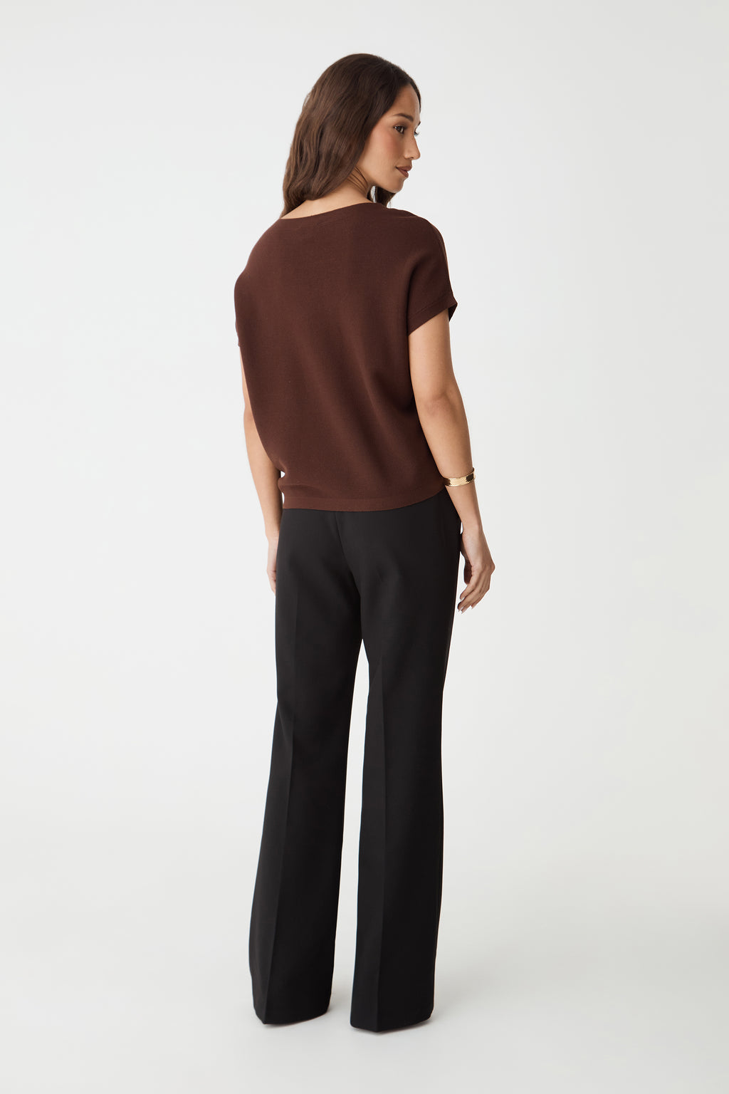 Back view of the Fudge brown knit top with ribbed hem band, worn with black trousers