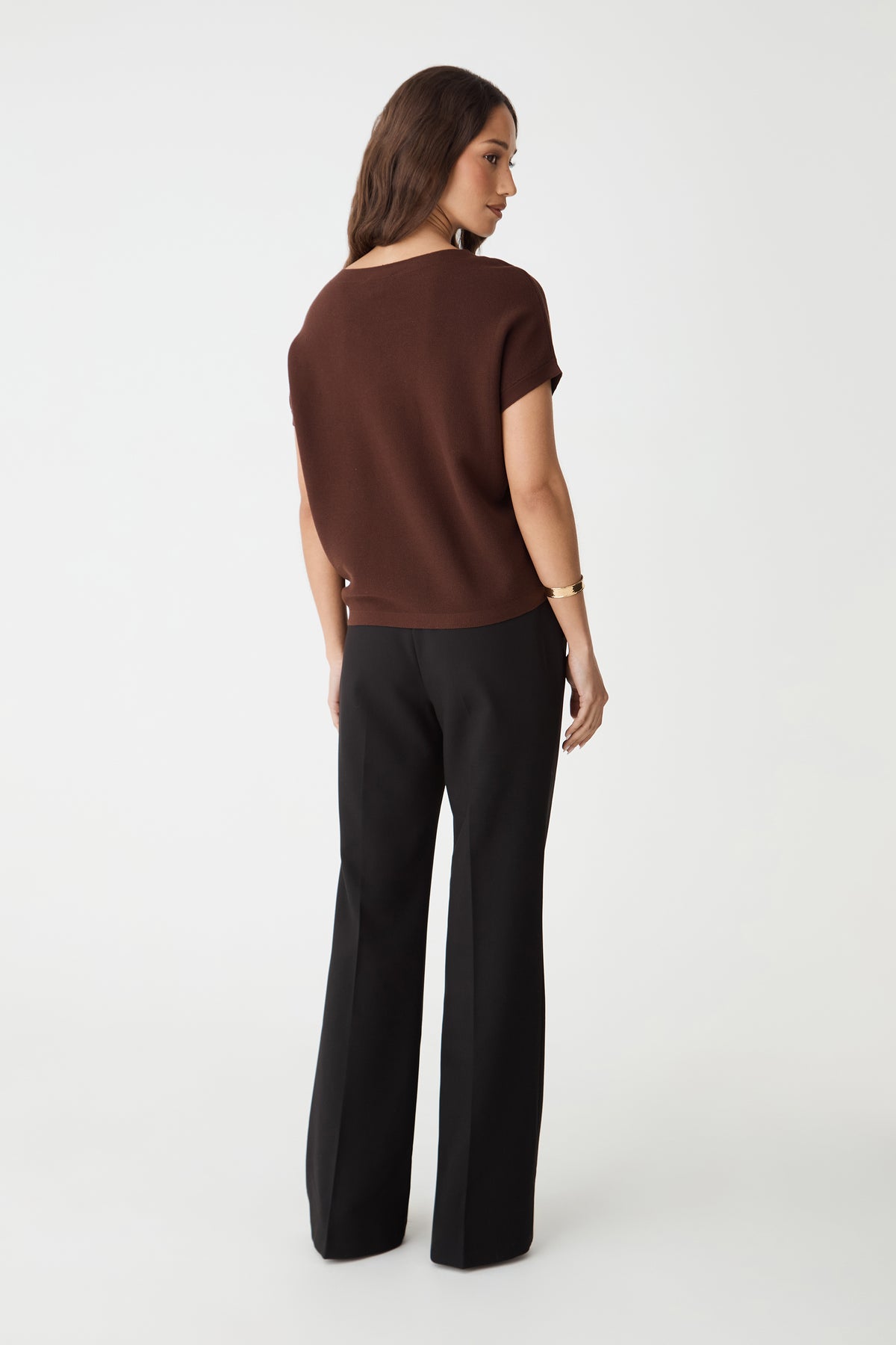Back view of the Fudge brown knit top with ribbed hem band, worn with black trousers