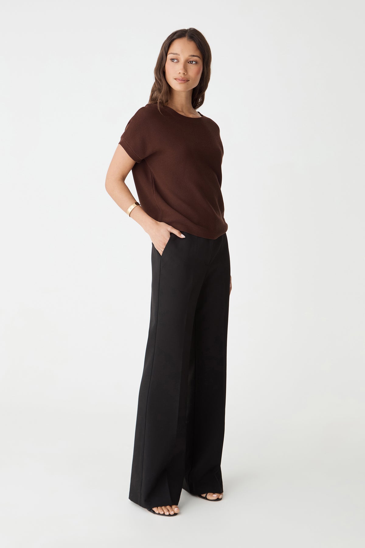 Side-on full-length view of the Fudge brown knit top with black wide-leg trousers