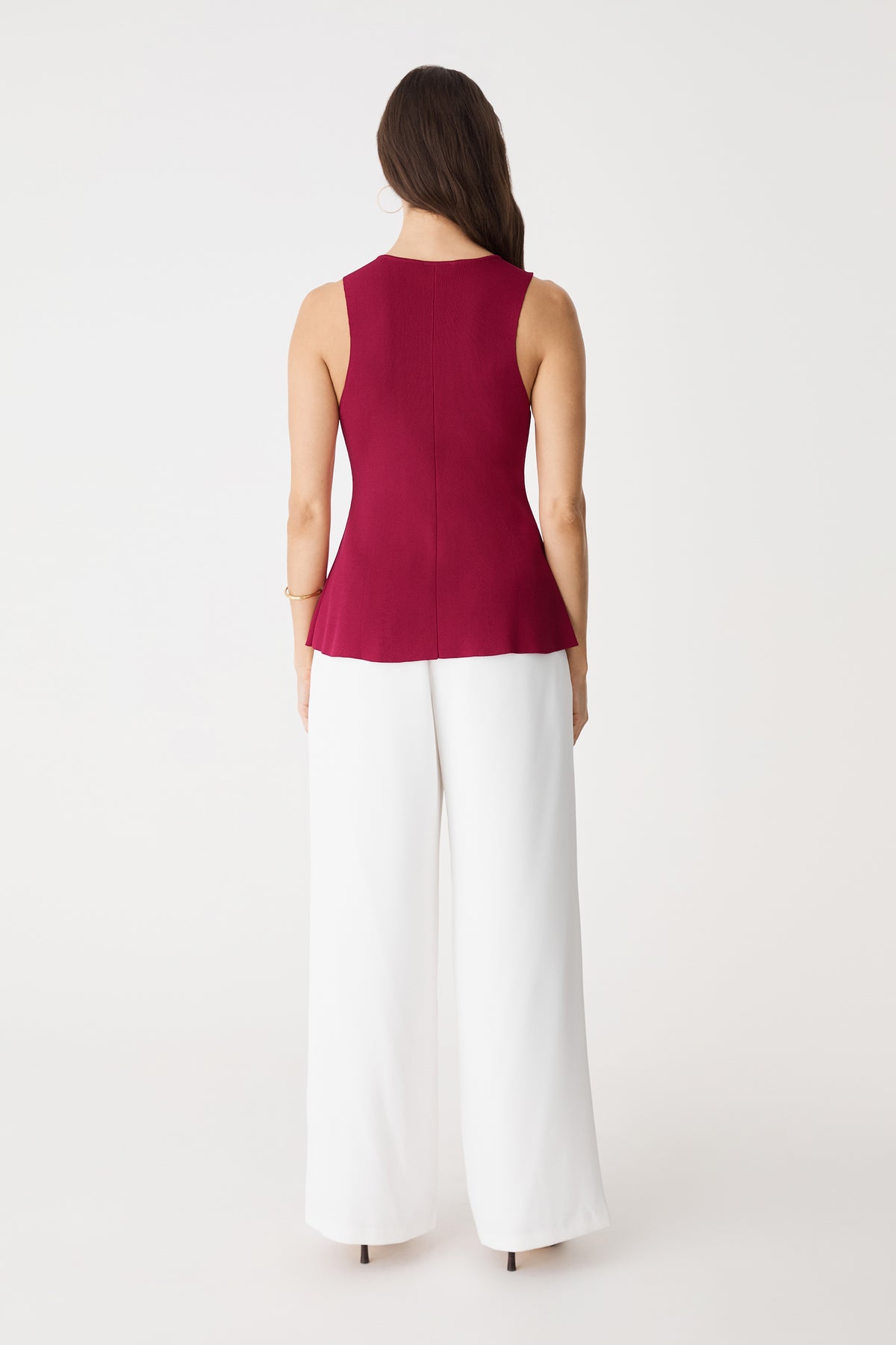 Back view of the fuchsia sleeveless peplum knit top with white trousers
