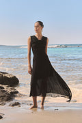 Desiree Asymmetric Skirt in black worn on the beach with a black sleeveless top, skirt blowing in the wind