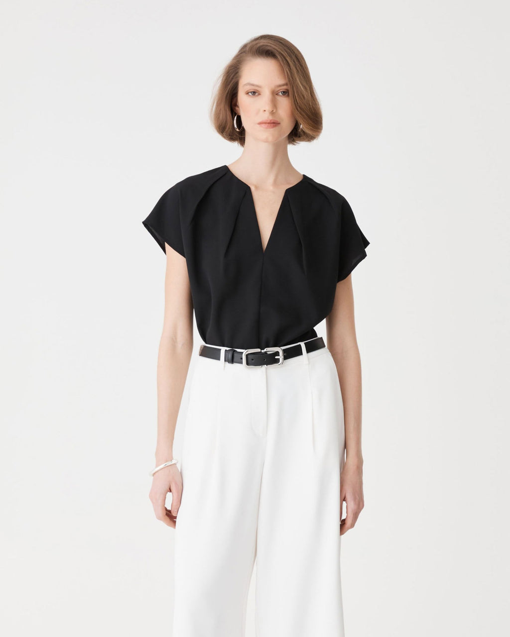 Jane Pleated Neck Top in black, front view with split V-neckline and cap sleeves, worn with white wide-leg trousers