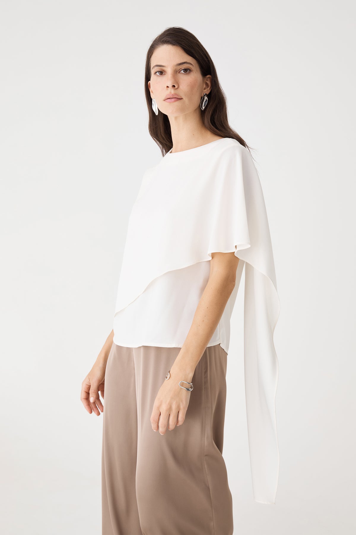 Side view showing the draped cape overlay and layered angular hem of the ivory top