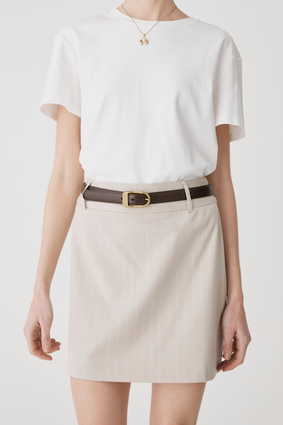 Rue Leather Belt in dark brown worn at the waist of a cream skirt with a white tee, front view