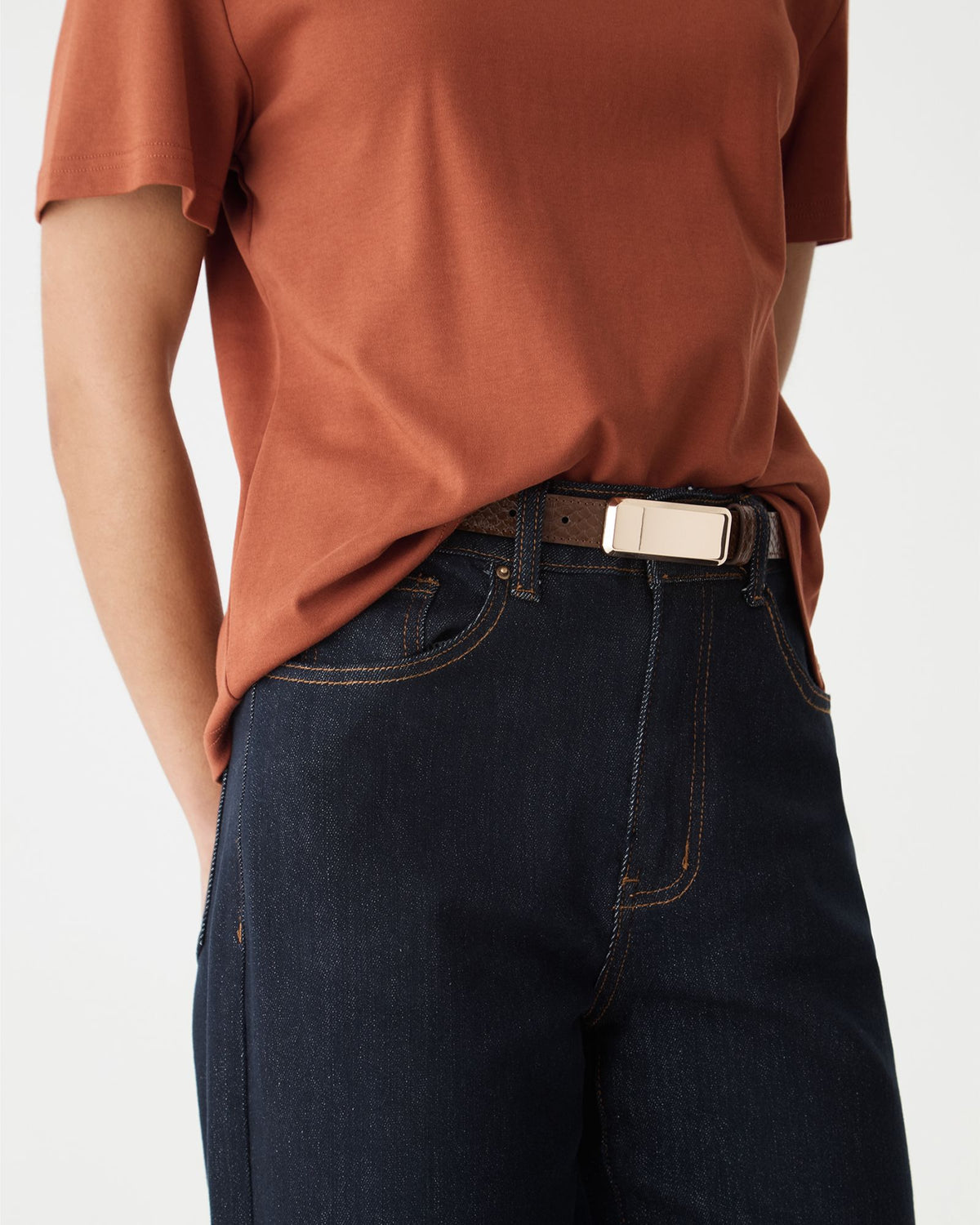 Side close-up of the belt buckle and croc-effect texture at the waist of dark jeans